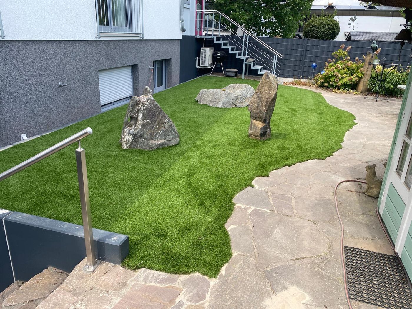 Kunstrasenfläche mit Findlingen neben einem Weg aus Natursteinplatten