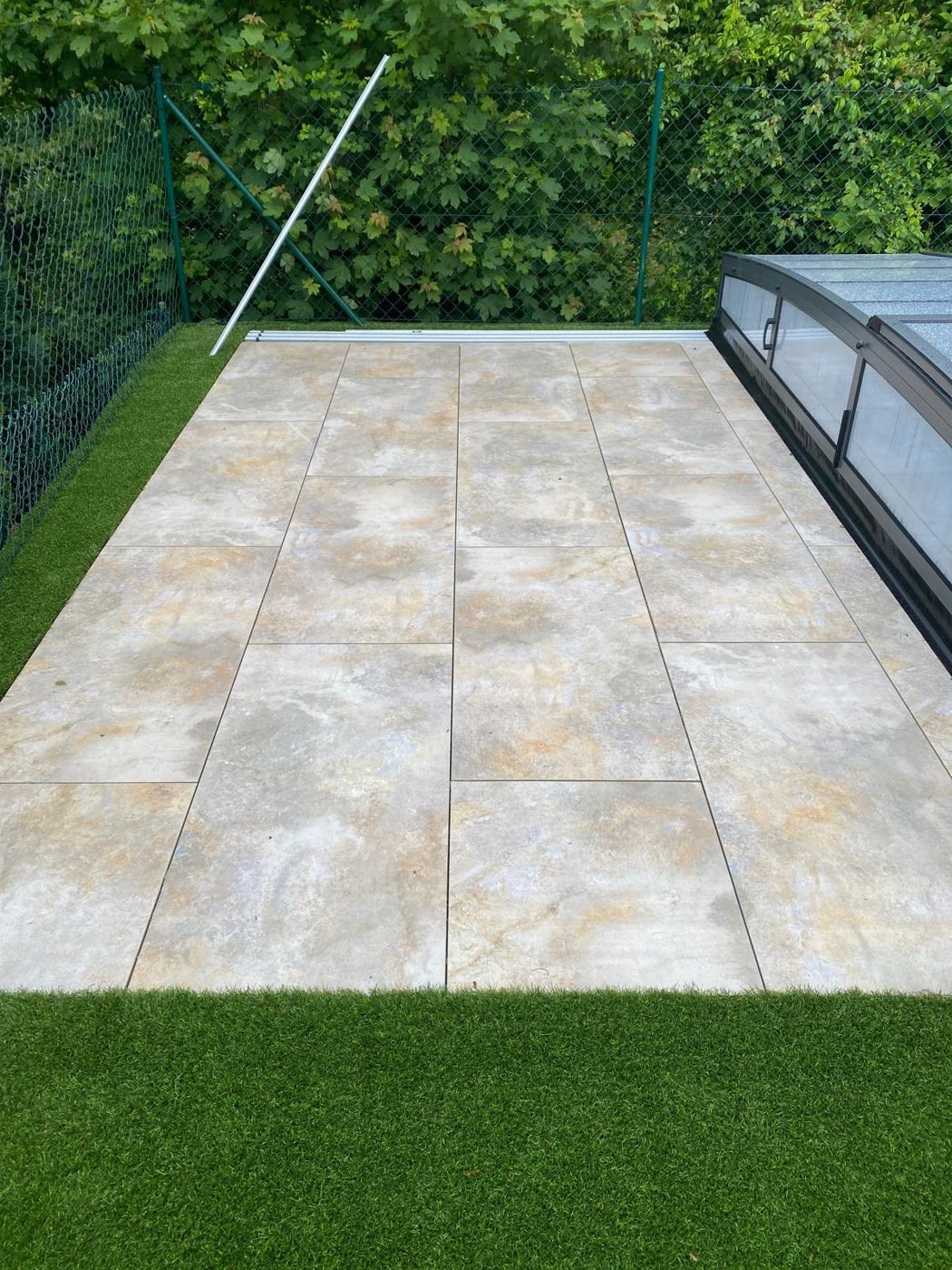 Terrasse aus großformatigen Keramikplatten in Steinoptik neben einem Pool, eingefasst von Kunstrasen