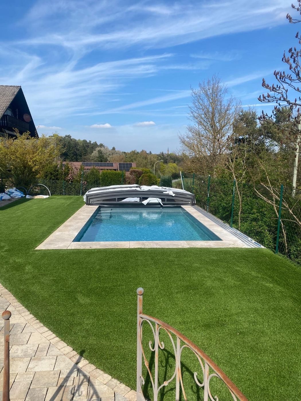 Pool mit Abdeckung in einem Hanggarten, umgeben von Kunstrasen